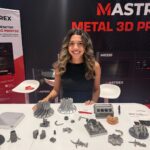 CEA Staffing trade show representative at a booth at IMTS 2026 in Chicago, smiling behind a table of metal 3D printed parts