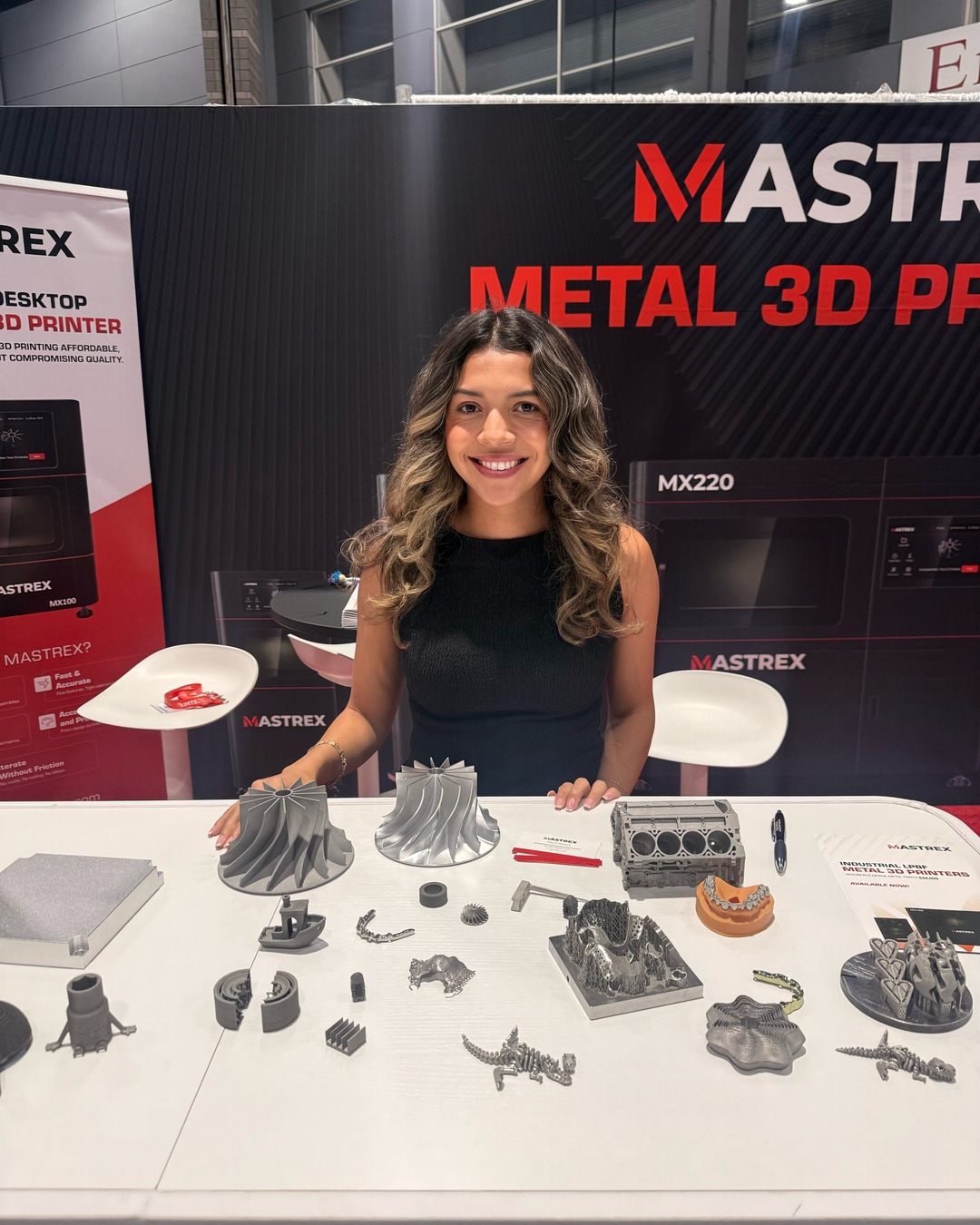 CEA Staffing trade show representative at a booth at IMTS 2026 in Chicago, smiling behind a table of metal 3D printed parts